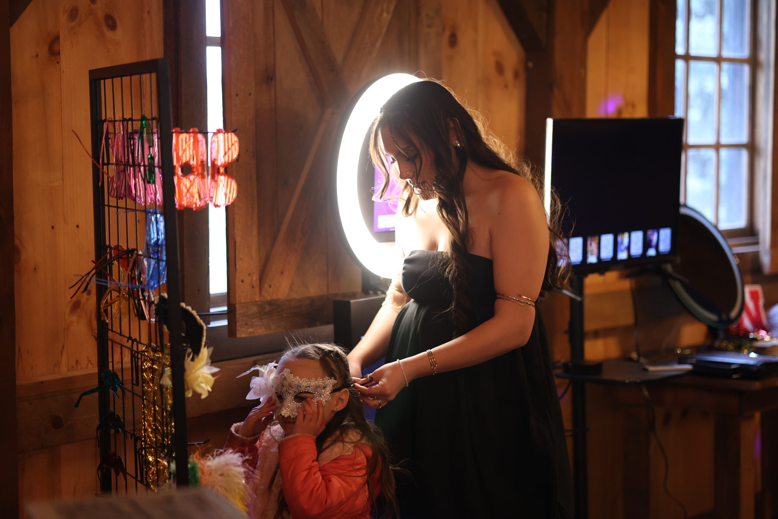 Mom putting on props for her daughter in front of photo booth stand